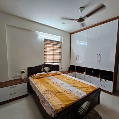 Dark carved-wood double bed under a yellow floral bedspread, facing a white gloss wardrobe whose drawer bank returns into the corner beside a zebra blind