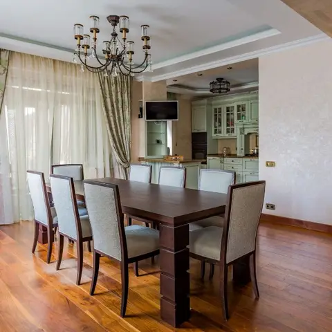 Dark wood dining table seating eight beneath a candelabra chandelier, floral drapery at the windows