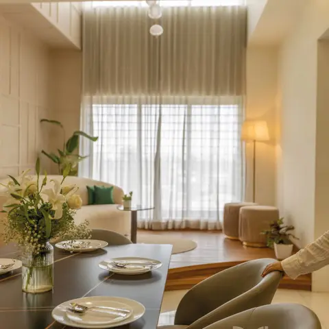 Dark wood dining table set for a meal in the foreground, opening onto a sunken living room with sheer floor-to-ceiling curtains and a cream sofa on a raised