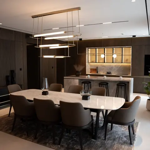 Dark wood-panelled dining and kitchen space with a marble oval table under a tiered brass-and-tube pendant chandelier