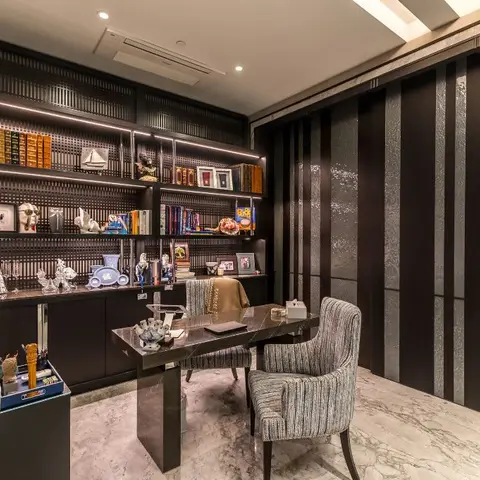 Dark wood-panelled study with backlit curio shelving, a glass-top desk, striped bouclé chairs, and a textured metallic accent wall.