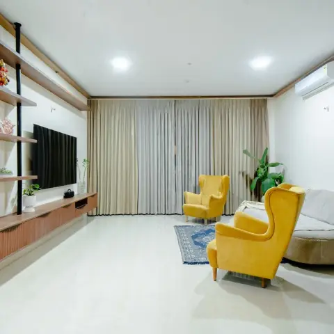 Daylit living room with a walnut floating TV console and black-rod open shelves holding a Ganesha idol and potted greens
