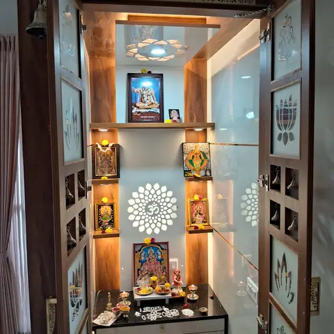 Dedicated pooja room with a carved wood temple unit, glass doors etched with deity motifs, a backlit white jaali Om medallion on the rear wall