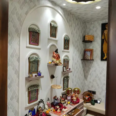 Dedicated pooja room with a tall arched niche wall of multiple deity photo frames and idols, patterned wallpaper