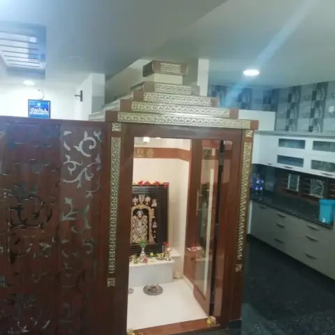 Dedicated pooja room with a tiered gold-trimmed wooden temple mandir and a carved wood jaali screen room divider, deity idols placed inside.