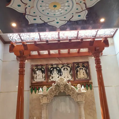 Dedicated pooja room with an ornate carved lotus ceiling medallion, a wood pergola-style entrance frame on turned pillars