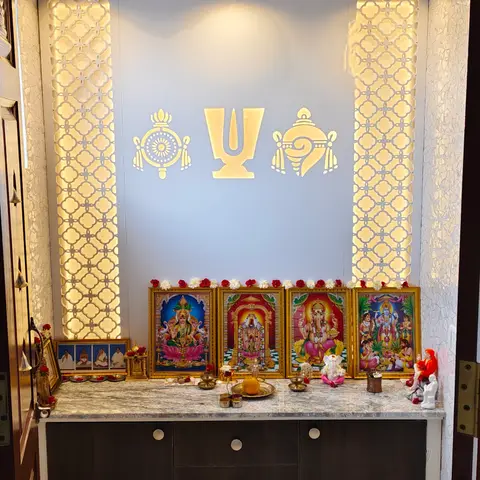 Dedicated pooja room with backlit CNC jaali side panels, a marble puja counter and a row of framed deity portraits.