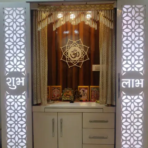 Dedicated pooja unit with backlit floral jaali side panels, an Om medallion backdrop, and cabinet storage below with deity idols on the ledge.