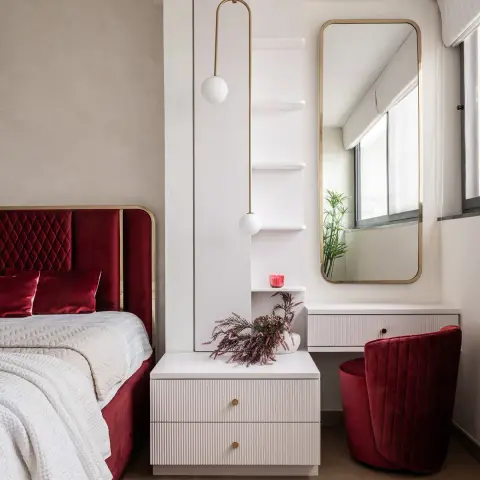 Deep red velvet diamond-tufted headboard with a brass edge sits beside a white fluted bedside chest
