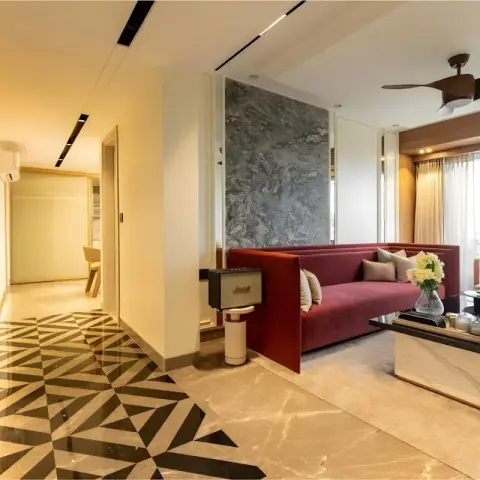 Deep-red velvet sofa set against a grey marble slab wall, with a black-and-cream geometric marble inlay running away down the passage and a grid of