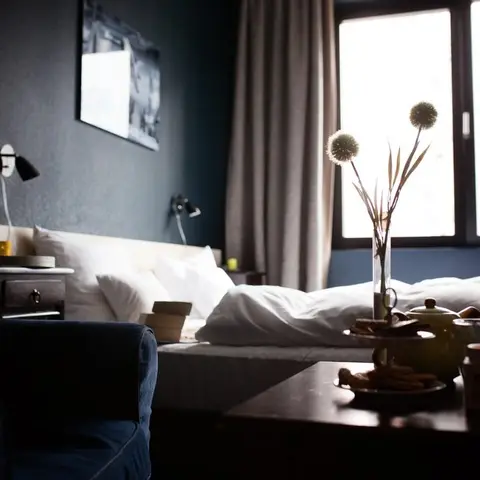Dim bedroom with a charcoal feature wall behind a low pale-wood platform bed, two black swing-arm reading lamps flanking the headboard