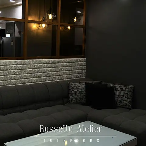 Dim living room with a dark grey tufted L-shaped sectional sofa against a white 3D brick-effect wall panel