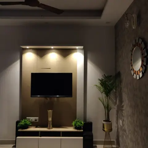 Dimly lit living room TV wall with a textured brown wallpaper panel, spotlighting on the TV, a sunburst mirror on the adjacent wallpapered wall