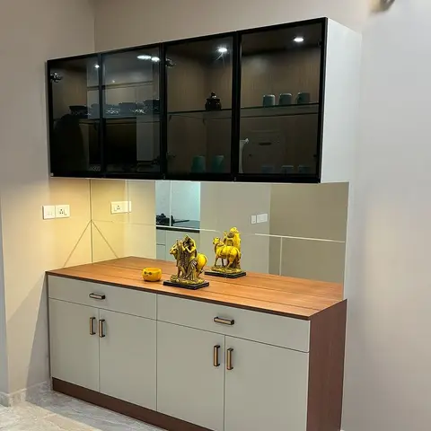 Dining-area crockery unit with a black-framed glass display cabinet above a mirrored backsplash and a two-tone wood-and-grey sideboard styled with brass