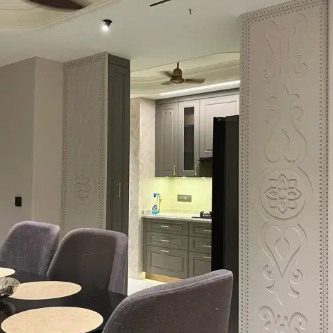 Dining area framed by tall carved relief-pattern wall panels, with a dark table and grey upholstered chairs opening into a grey shaker-style kitchen beyond