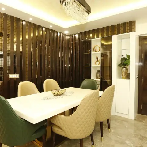 Dining area screened by a dark-wood vertical fin wall inset with bronze mirror strips, a white marble-top six-seater with green and beige quilted chairs