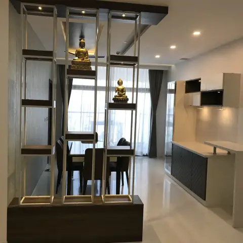 Dining area seen through a champagne-gold steel display screen carrying two gilded Buddha statues on wenge shelves