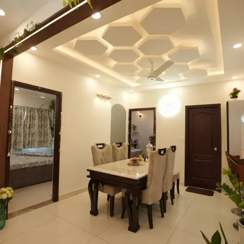 Dining area under a honeycomb-coffered POP ceiling with cove lighting, a marble-top six-seater on carved dark-wood legs with cream upholstered chairs