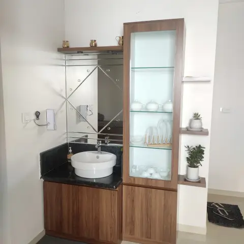 Dining-area wash counter in black granite with a bevelled-mirror splashback, butted against a tall walnut crockery unit with lit glass shelves holding white