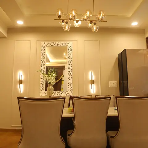 Dining area with a carved white-frame mirror flanked by wall sconces, wood floor, and a smoked-glass cabinet opening to the kitchen.