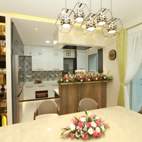 Dining area with a geometric honeycomb pendant light cluster over a marble-top table, a built-in bar display shelf, and an open kitchen beyond.