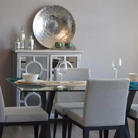 Dining area with a glass-top table set for a meal, upholstered chairs on black legs