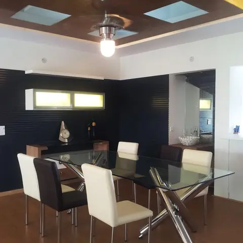 Dining area with a glass-top chrome-cross-leg table, cream and brown leather chairs, a dark ribbed accent wall with a backlit display shelf