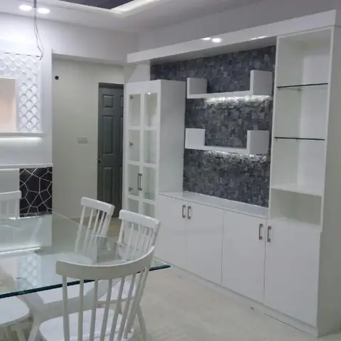 Dining area with a glass-top table seating six, a white crockery display unit with a charcoal mosaic tile backdrop and glass shelving