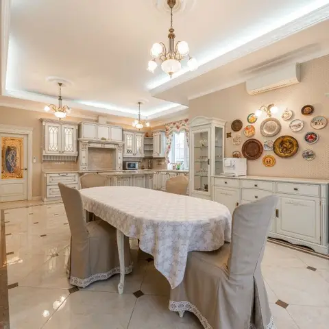 Dining area with a linen-draped table and skirted chairs, ornate chandeliers, a glass-front display cabinet