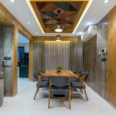 Dining area with a live-edge wood table and black leather chairs beneath a geometric wood-inlay ceiling feature and pendant lights, flanked by stone-clad walls.