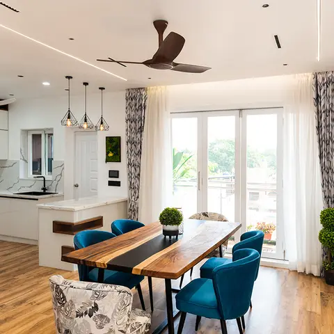 Dining area with a live-edge wood-and-black-resin table, teal velvet chairs and black wire-cage pendant lights