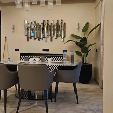 Dining area with a marble-top table and grey leather chairs beneath a linear acrylic-drop pendant