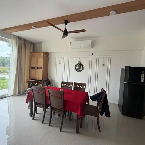 Dining area with a six-seater wood table draped in a red tablecloth, a carved wooden wardrobe with brass inlay against the wall