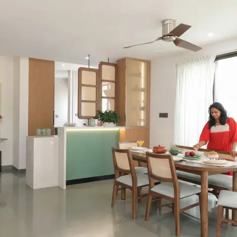 Dining area with a six-seater teak table and cane-back chairs, a cane-and-fluted-glass crockery tower next to a mint-green breakfast counter