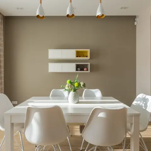 Dining area with a taupe accent wall, three cone pendant lights over a white table with Eiffel-style chairs