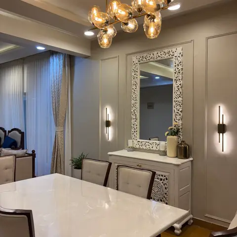 Dining area with a white marble-top table, upholstered dining chairs, an ornate carved mirror over a console, and a cluster glass-globe chandelier.