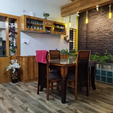 Dining area with a wood table and dark chairs facing a textured dark slate feature wall strung with pendant bulbs, next to a glass-block water panel.