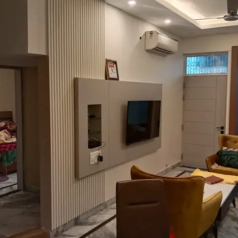 Dining corner facing a beige TV panel with a lit glass-shelf niche, set against floor-to-ceiling white fluted panelling