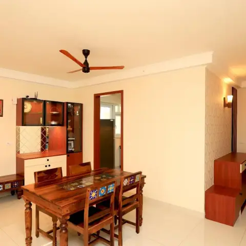 Dining corner of an Indian flat with a sheesham six-seater and a matching low bench, both inlaid with blue-and-yellow ceramic tiles