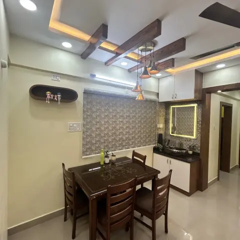 Dining corner under a grid of dark faux-wood beams set into a cove-lit ceiling, with a cluster of copper cone pendants over a four-seater teak table
