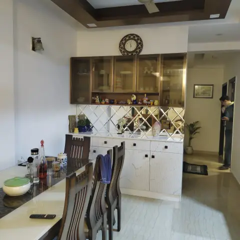 Dining corner with a glass-front crockery unit over a diamond-bevelled mirror backsplash and marble-look base cabinets, a filigree wall clock