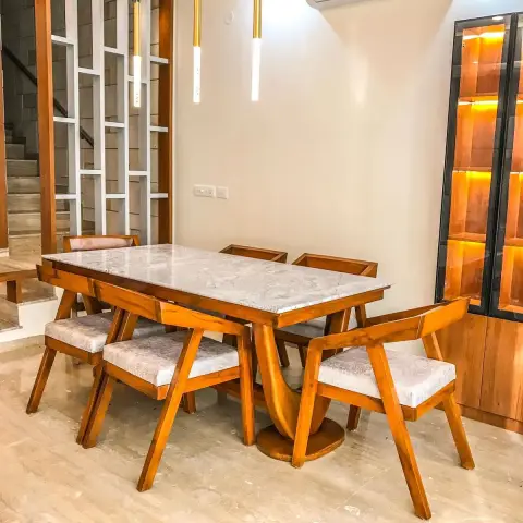 Dining corner with a marble-topped teak table on a sculpted pedestal and four teak armchairs, three slim brass cylinder pendants