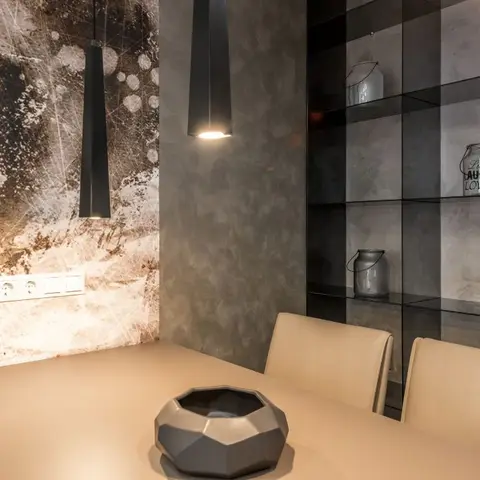 Dining corner with a moody abstract textured accent wall, slim black pendant lights, and a smoked-glass display shelf styled with decor jars
