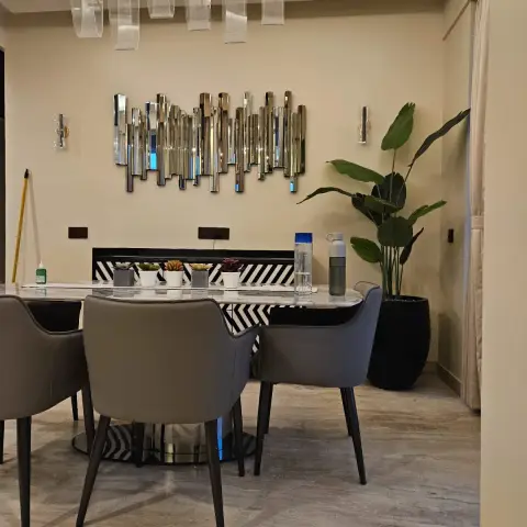 Dining corner with an oval marble-top table on a brushed-gold drum base and taupe leather tub chairs, a linear glass-blade suspension