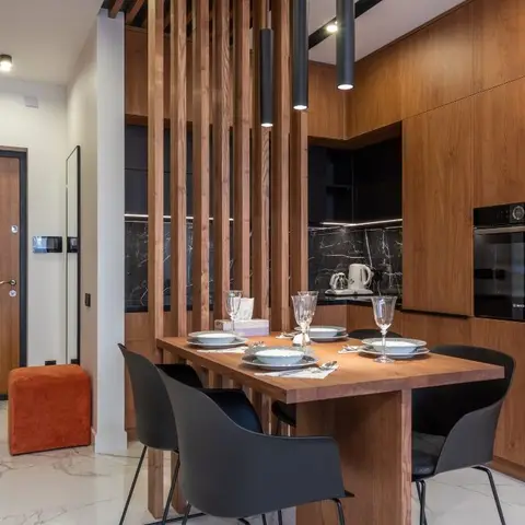 Dining nook set for a meal behind a vertical wood-slat screen divider, with a wood-panelled kitchen wall and built-in oven visible behind