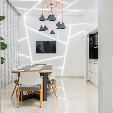 Dining nook under a faceted white ceiling and wall lit with embedded linear LED strips