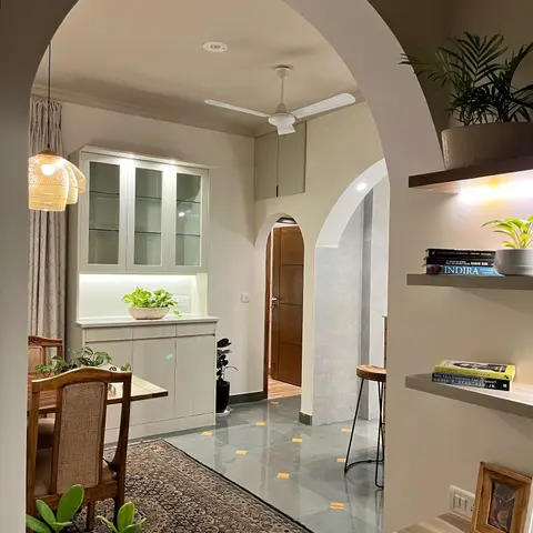 Dining nook viewed through an arched doorway, with a rattan pendant light, a glass-front crockery cabinet, cane dining chairs and a patterned rug.
