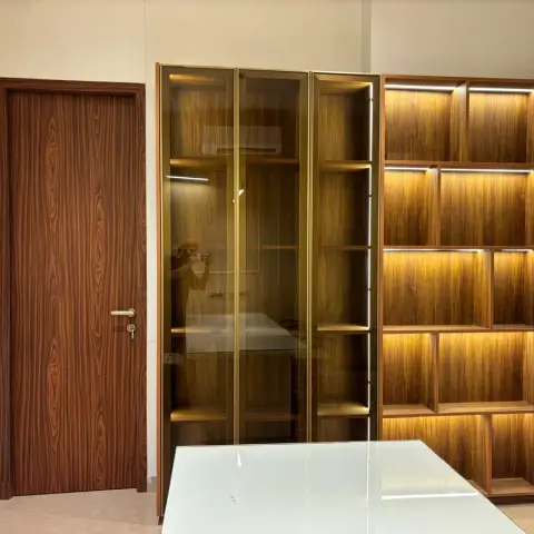 Dining nook wall with a backlit walnut display shelving unit, a gold-framed glass cabinet section