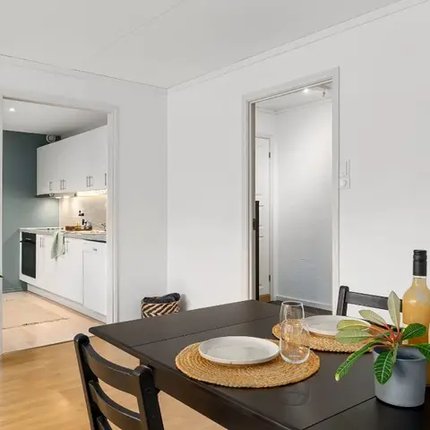 Dining nook with a black table and woven placemats opening through white doorways to a small galley kitchen and a hallway.