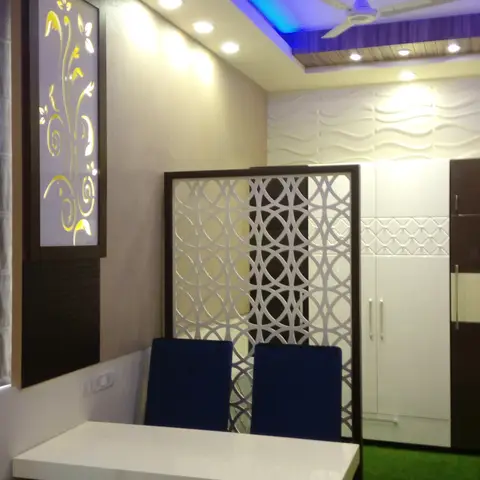 Dining nook with a blue-lit cove ceiling, backlit yellow floral jaali panel, and a laser-cut circular-pattern partition screen behind navy dining chairs